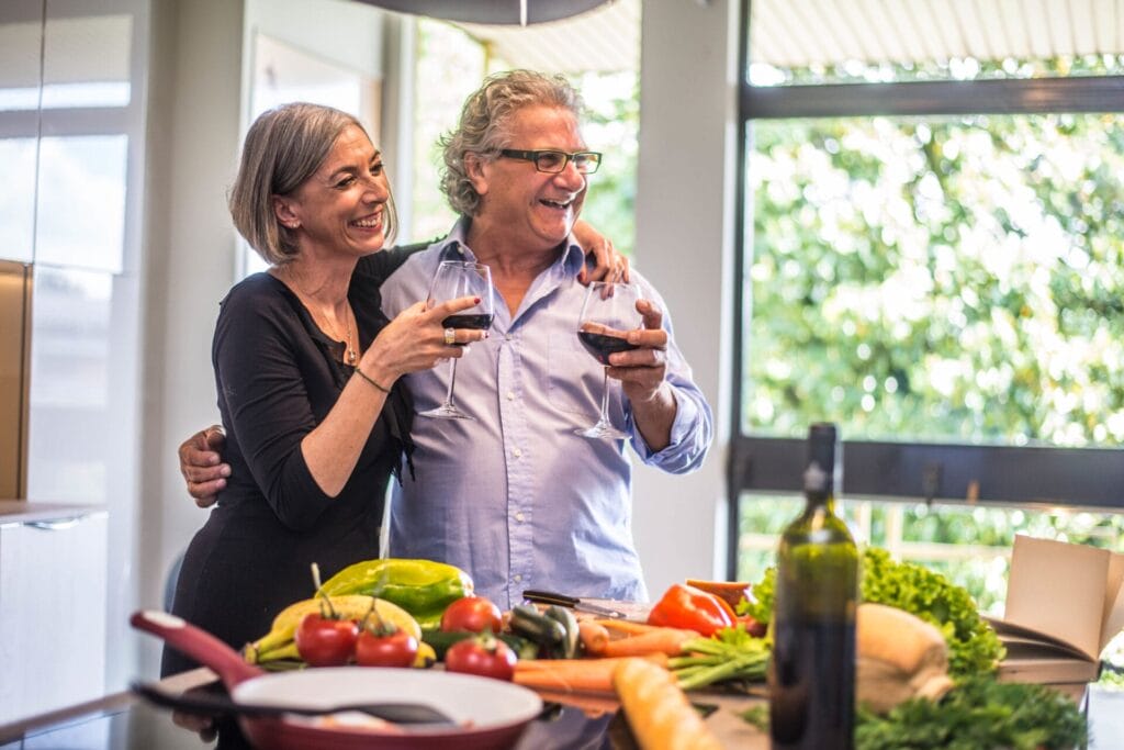 Senior couple cooking healthy food and drinking red wine at house kitchen