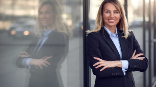 Single confident and attractive female businesswoman in blue suit with grin leaning on window outdoors