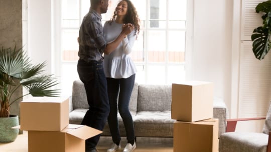 Happy African American couple in love dancing after moving in new house, attractive smiling woman and man celebrating relocating, cardboard boxes with belongings, homeowners in new apartment